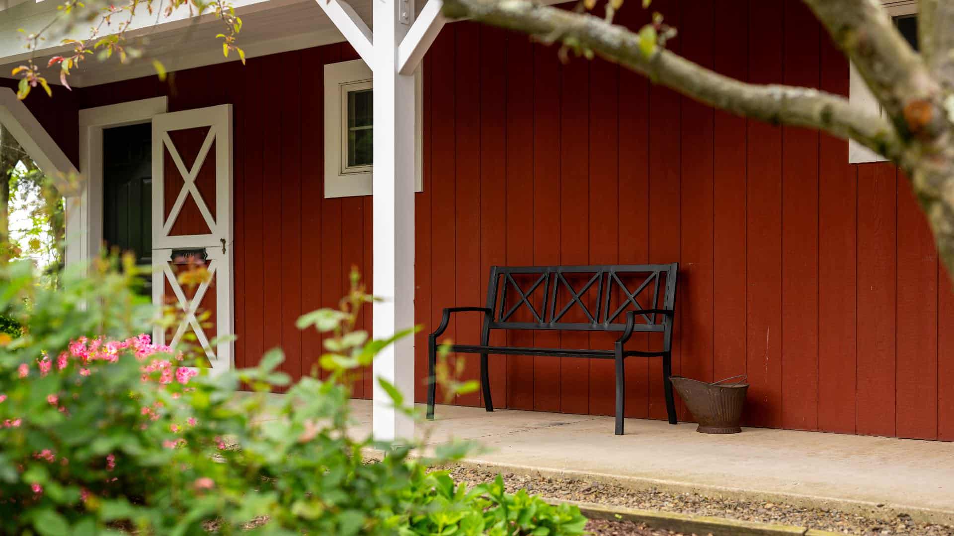 Exterior view of property painted red with white trim, barn-like door, and black metal bench