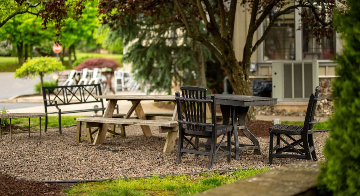 Picnic area near property nestled under trees with a wooden picnic table and dark wooden table and chairs