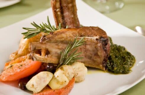 Close up view of a dinner dish with lamb chops and vegetables on a white square place