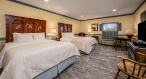 Bedroom with cream walls, blueish gray trim, two beds each with a dark wooden headboard and white and blue bedding, and dark wooden desk and chair