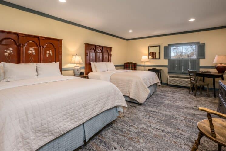 Bedroom with cream walls, blueish gray trim, two beds each with a dark wooden headboard and white and blue bedding, and dark wooden desk and chair