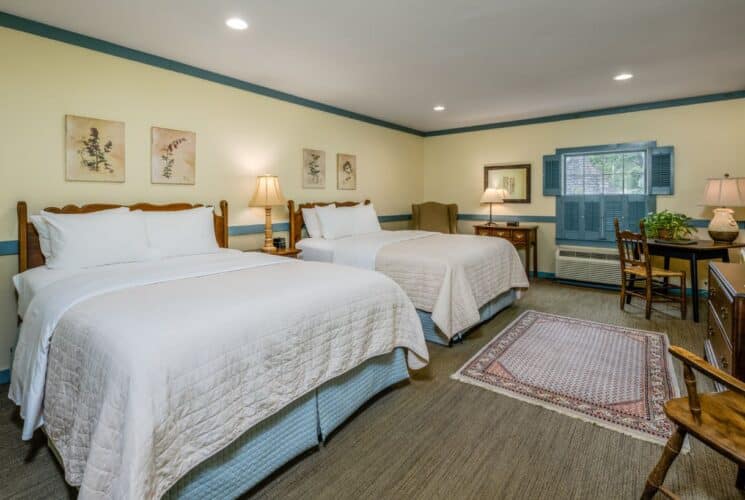 Bedroom with cream walls, blueish gray trim, two beds each with a dark wooden headboard and white and blue bedding, and dark wooden desk and chair