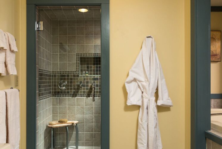 Bathroom with yellow walls, sage trim, walk in tile shower with glass door, and white robe hanging on a hook on the wall