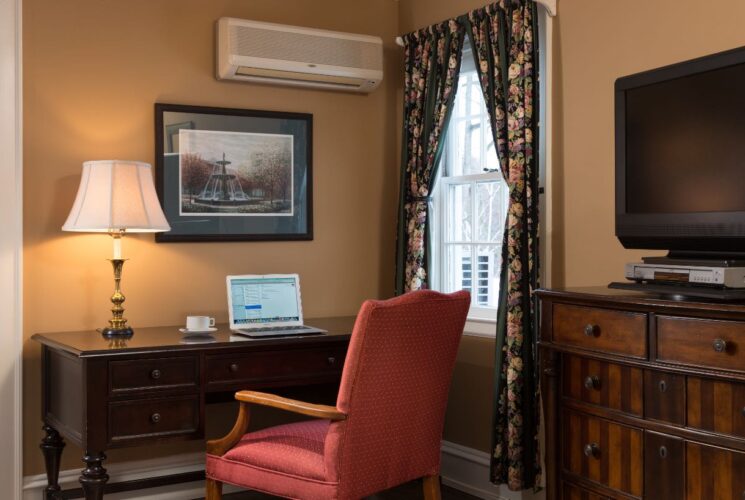 Bedroom with light caramel walls, white trim, hardwood flooring, dark wooden desk, upholstered chair, and dark wooden dresser with a TV on top