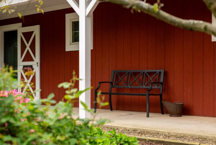 Exterior view of property painted red with white trim, barn-like door, and black metal bench