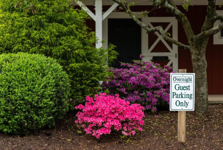 Exterior view of property painted red with white trim and barn-like door with large green bushes, a pink-flowering bush, and a purple-flowering bush