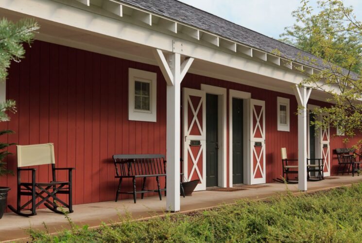 Exterior view of property painted red with white trim, barn-like doors, and many wooden benches and chairs