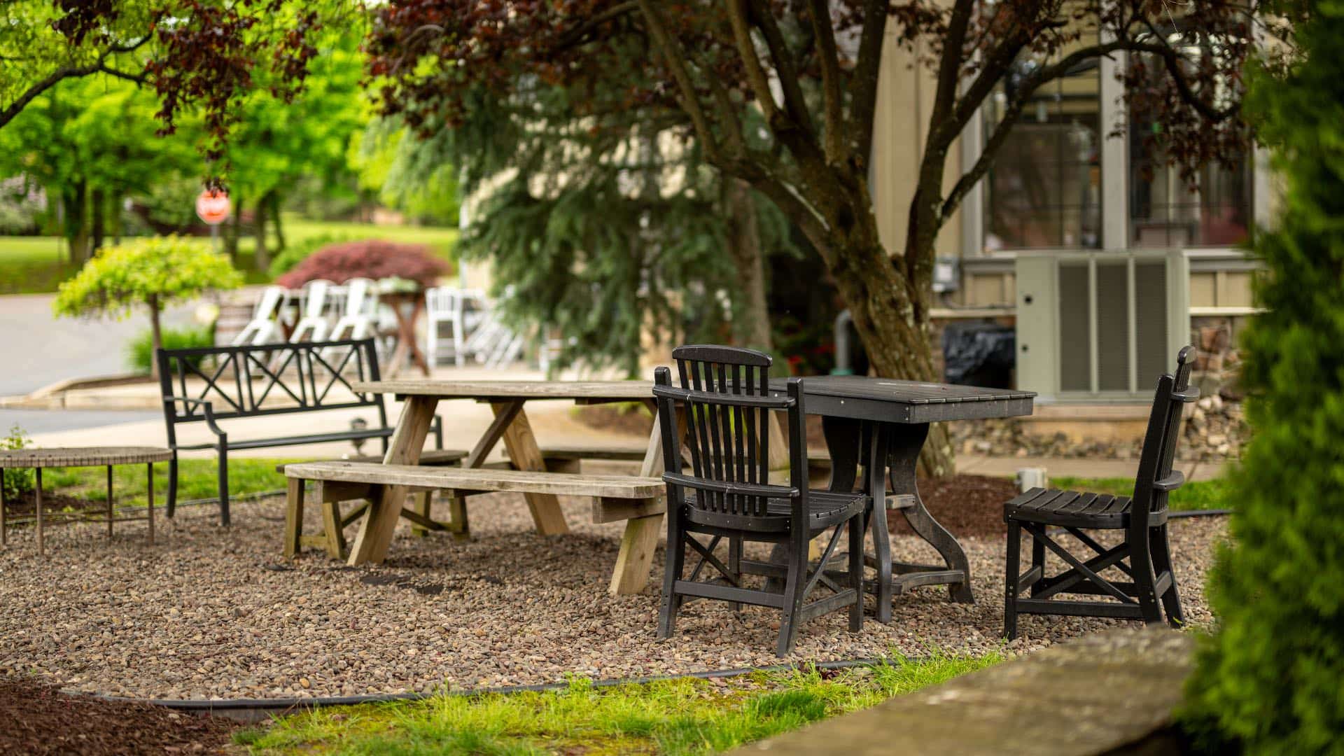 Picnic area near property nestled under trees with a wooden picnic table and dark wooden table and chairs