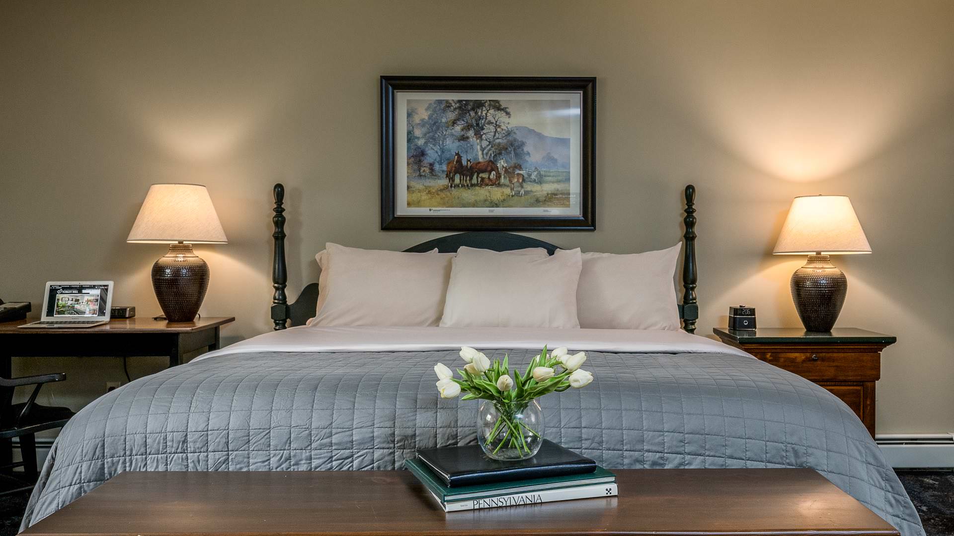 Bedroom with light cream walls, white trim, dark wooden headboard, white and blue bedding, and dark wooden desk and chair