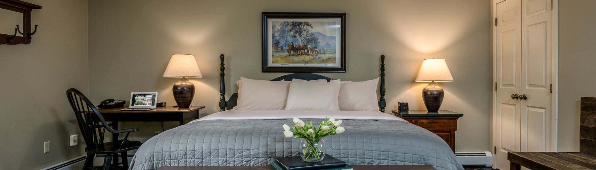 Bedroom with light gray walls, white trim, dark wooden headboard, white and blue bedding, and dark wooden desk and chair