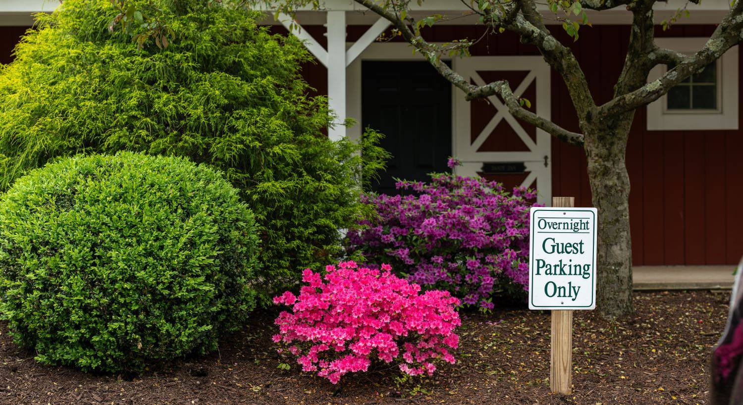 Exterior view of property painted red with white trim and barn-like door with large green bushes, a pink-flowering bush, and a purple-flowering bush