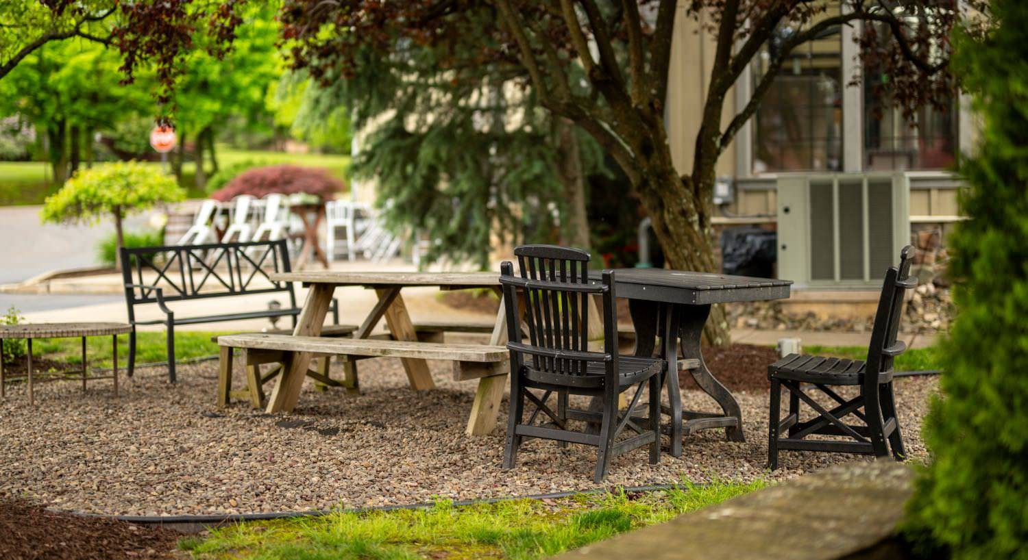 Picnic area near property nestled under trees with a wooden picnic table and dark wooden table and chairs