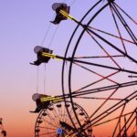 View of multiple Ferris wheel rides lit by a sunset