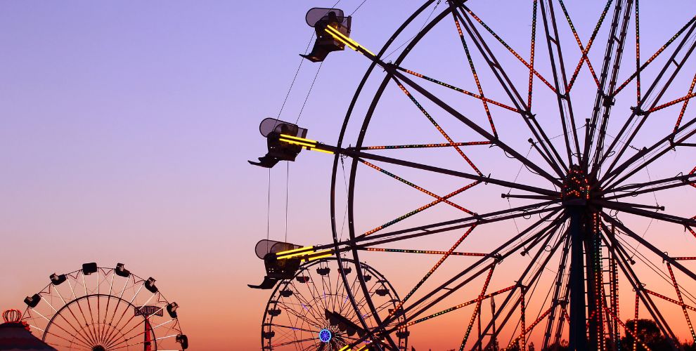 View of multiple Ferris wheel rides lit by a sunset