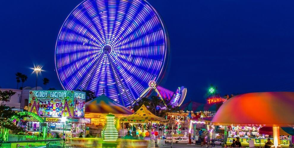 Bright lights of booths, games, and ferris wheel of a carnival at night