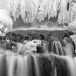 water flows under a frozen waterfall