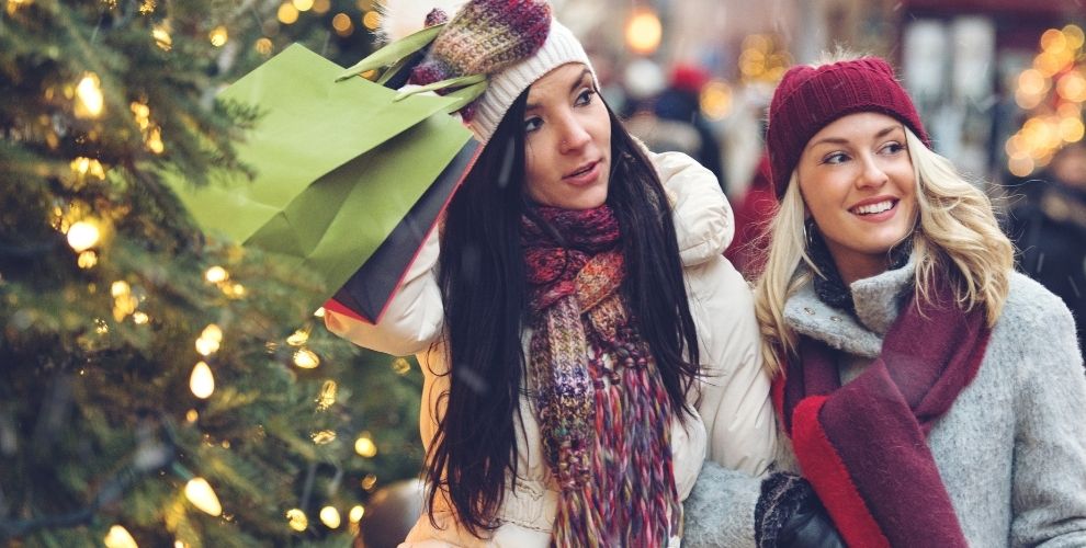 two ladies dressed warmly holding shopping bags and smiling looking at various shops